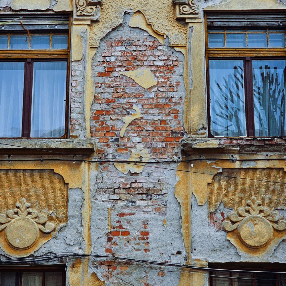 Fațadă degradată de clădire istorică, cu tencuială căzută și ornamente vechi